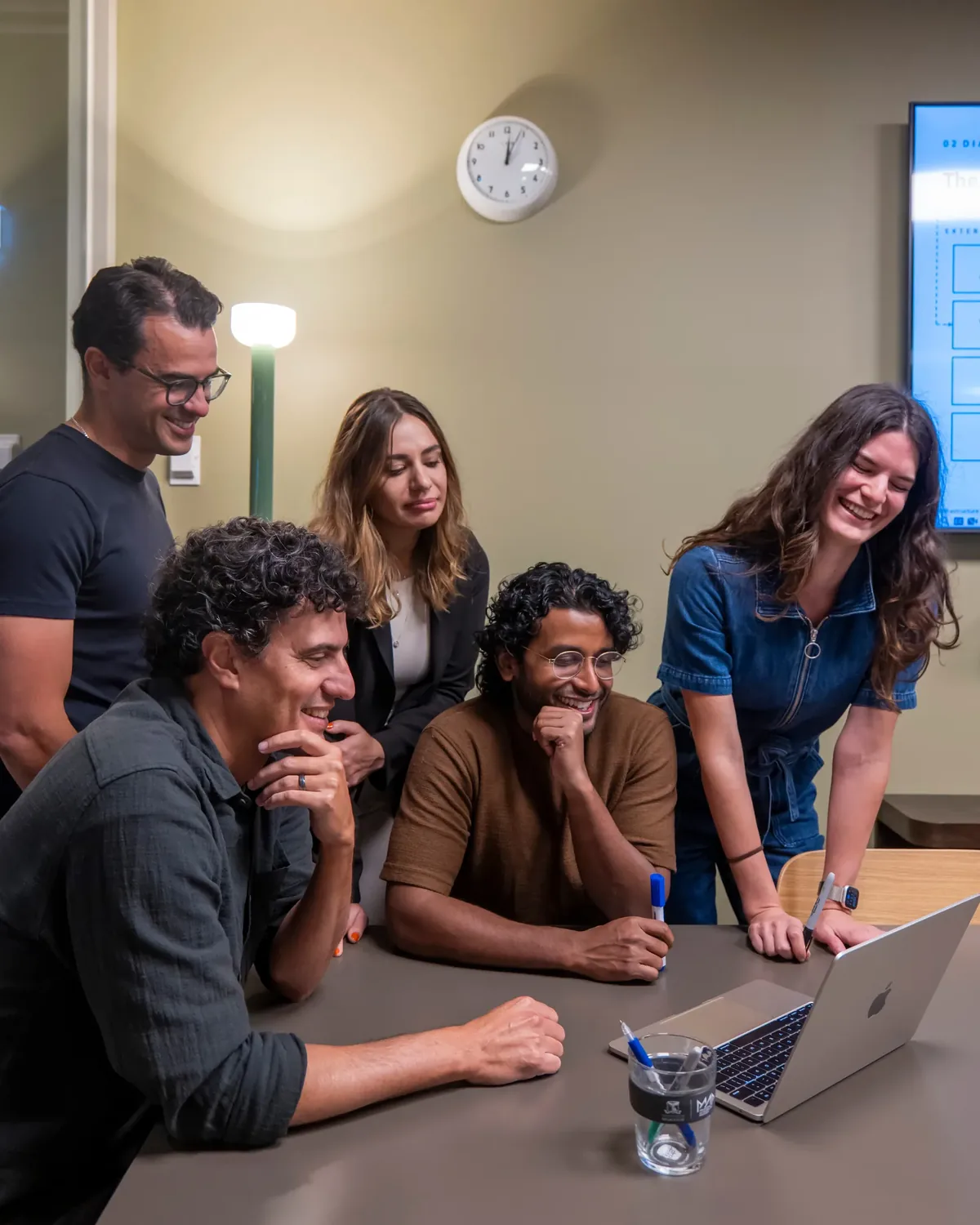 Five of the Mayfly team gathered around a laptop, working through something together